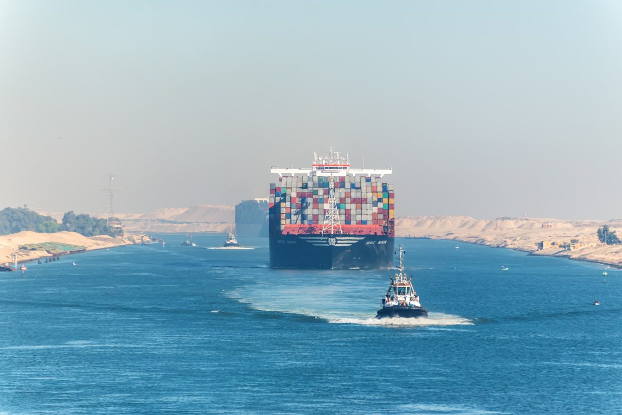 Ismailia, Egypt - November 5, 2017: Large container vessel ship MSC Maya passing Suez Canal in the sandy haze in Egypt. Tugboat accompanies the ships.