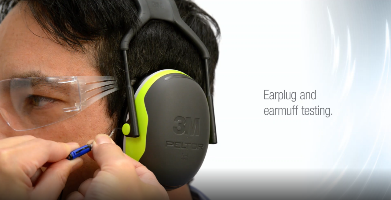 Man with dark hair and safety goggles, with 3M earmuffs demonstrating ear protection